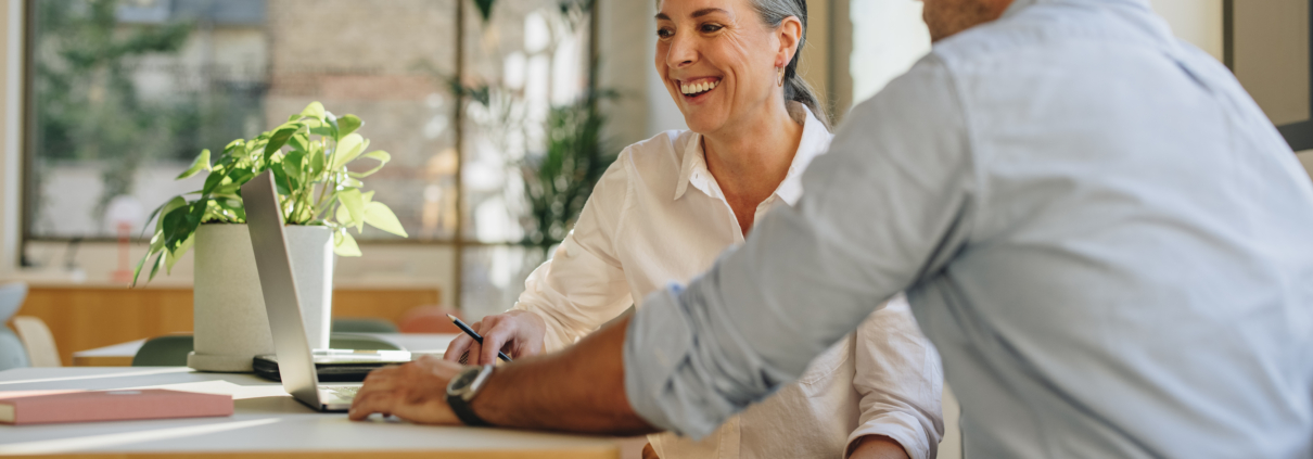 A man and a woman with a laptop, meeting in an office, are negotiating cooperatively, the woman is smiling.