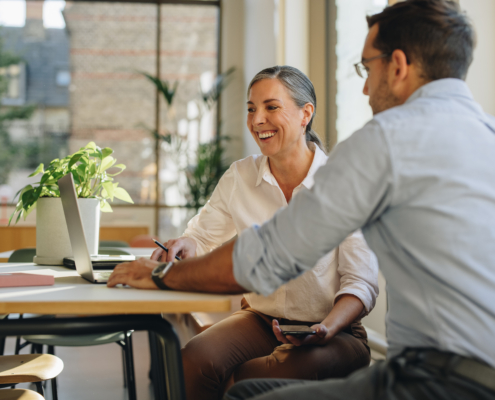 A man and a woman with a laptop, meeting in an office, are negotiating cooperatively, the woman is smiling.